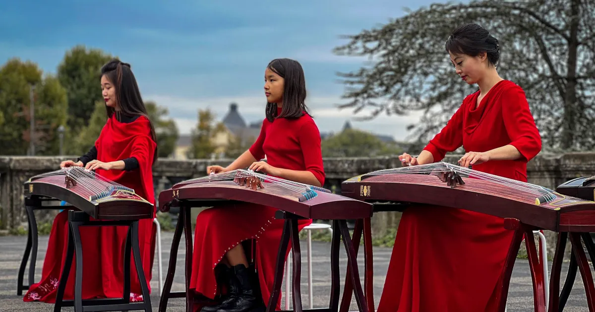 Three guzheng players in red dresses performing side by side outdoors