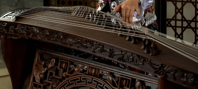 Close-up of a carved wooden guzheng body, its strings and bridges
