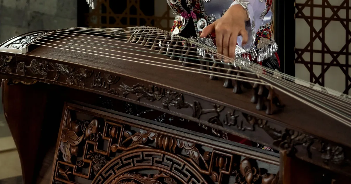 Close-up of a carved wooden guzheng body, its strings and bridges