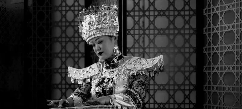 Black-and-white photo of a guzheng player in an ornate silver headdress and traditional costume