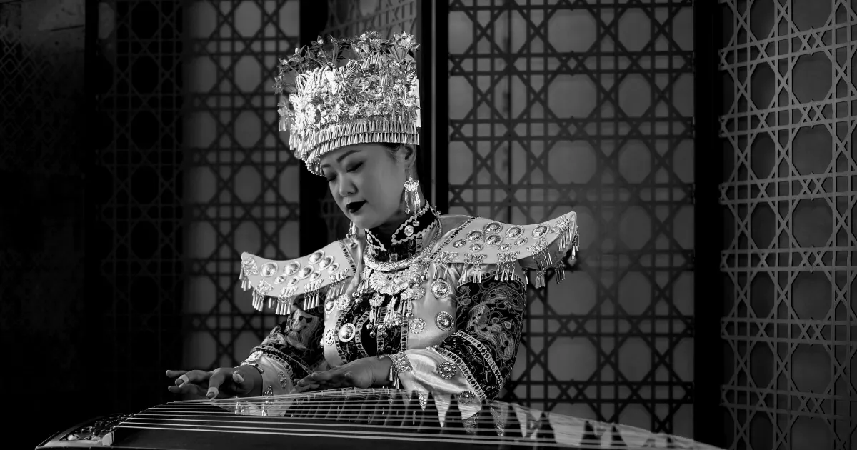 Black-and-white photo of a guzheng player in an ornate silver headdress and traditional costume