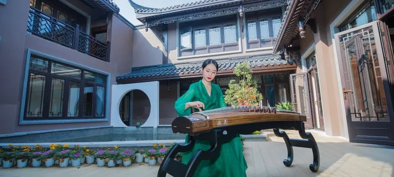 A guzheng player in a green dress performing in a traditional Chinese courtyard