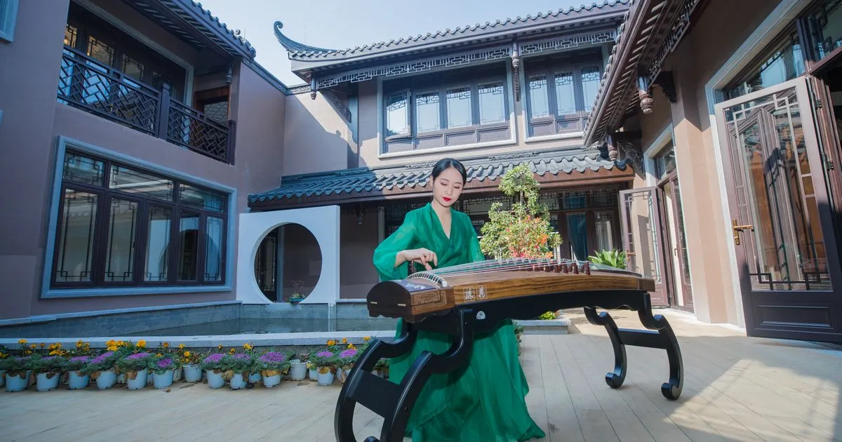 A guzheng player in a green dress performing in a traditional Chinese courtyard